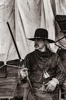 Old Time Cowboy Black and White Sepia Print. Plainsman with Henry Rifle at wagon.