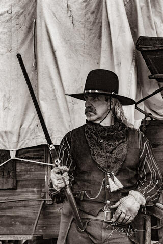 Old Time Cowboy Black and White Sepia Print. Plainsman with Henry Rifle at wagon.