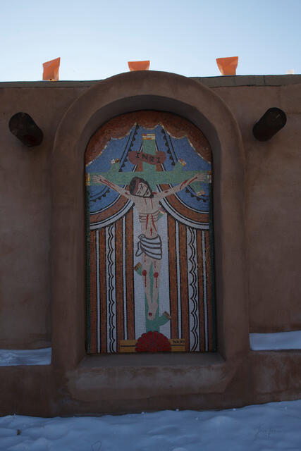 Fine art photography by Jess R. Lee of a religious mosaic crucifixion in an adobe archway surrounded by snow in New Mexico.