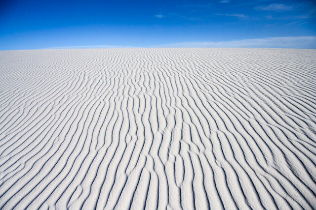 Luxury wall art of the New Mexico desert. A wide-angle landscape photograph showcasing the rhythmic, wind-swept ridges of white sand dunes under clear blue sky