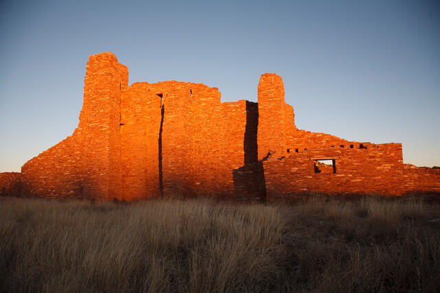 Fine art photography by Jess R. Lee of the ancient red stone ruins of Abo Pueblo Mission glowing in the orange light of a New Mexico sunset.