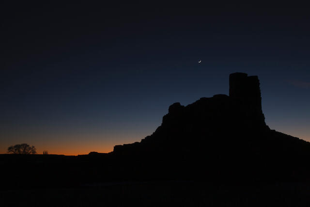 Fine art night photography by Jess R. Lee of a crescent moon over a silhouetted desert mesa in New Mexico.