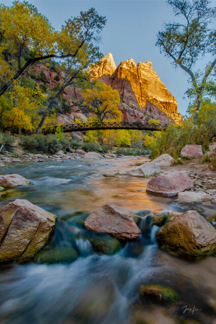 Vertical landscape photo print of the Virgin River flowing over rocks under a bridge toward the glowing orange peak of The Sentinel in autumn.