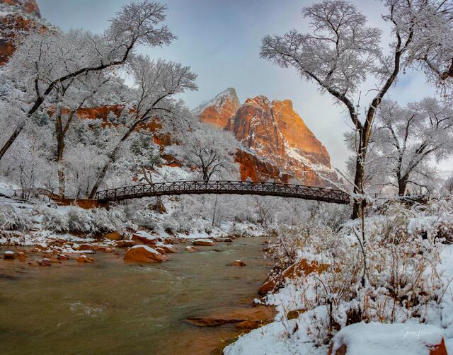 Zion Landscape photo print of a snow-covered bridge over the Virgin River leading toward a glowing red mountain peak in winter.