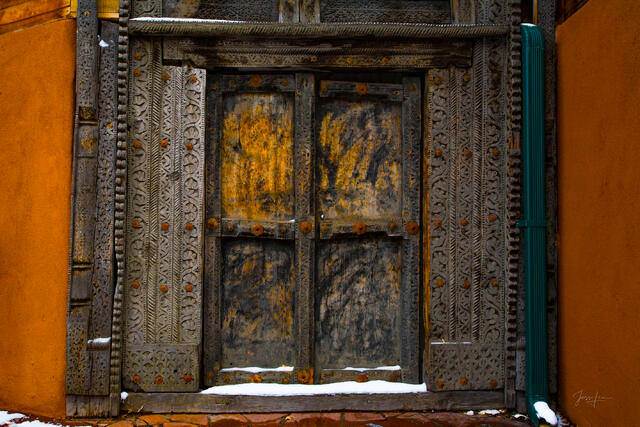 Luxury wall art of a historic Santa Fe architectural entry showcasing a large, dark brown quartered door set within an intricately carved, weathered frame