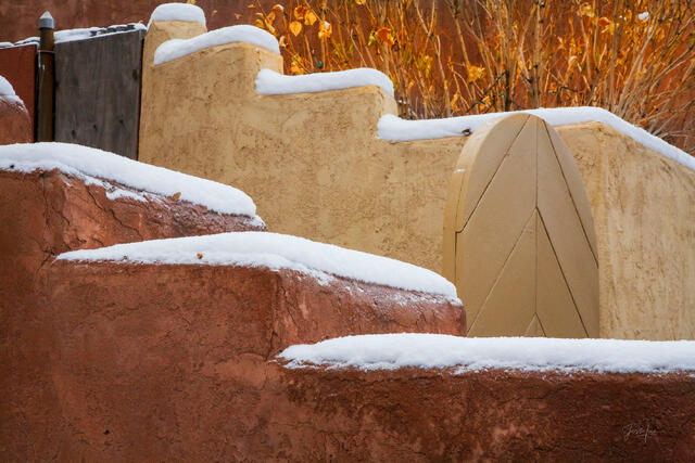 Fine art photography print of a snow-capped adobe staircase in Santa Fe, New Mexico, featuring vibrant red steps, light adobe walls, and the soft textures.