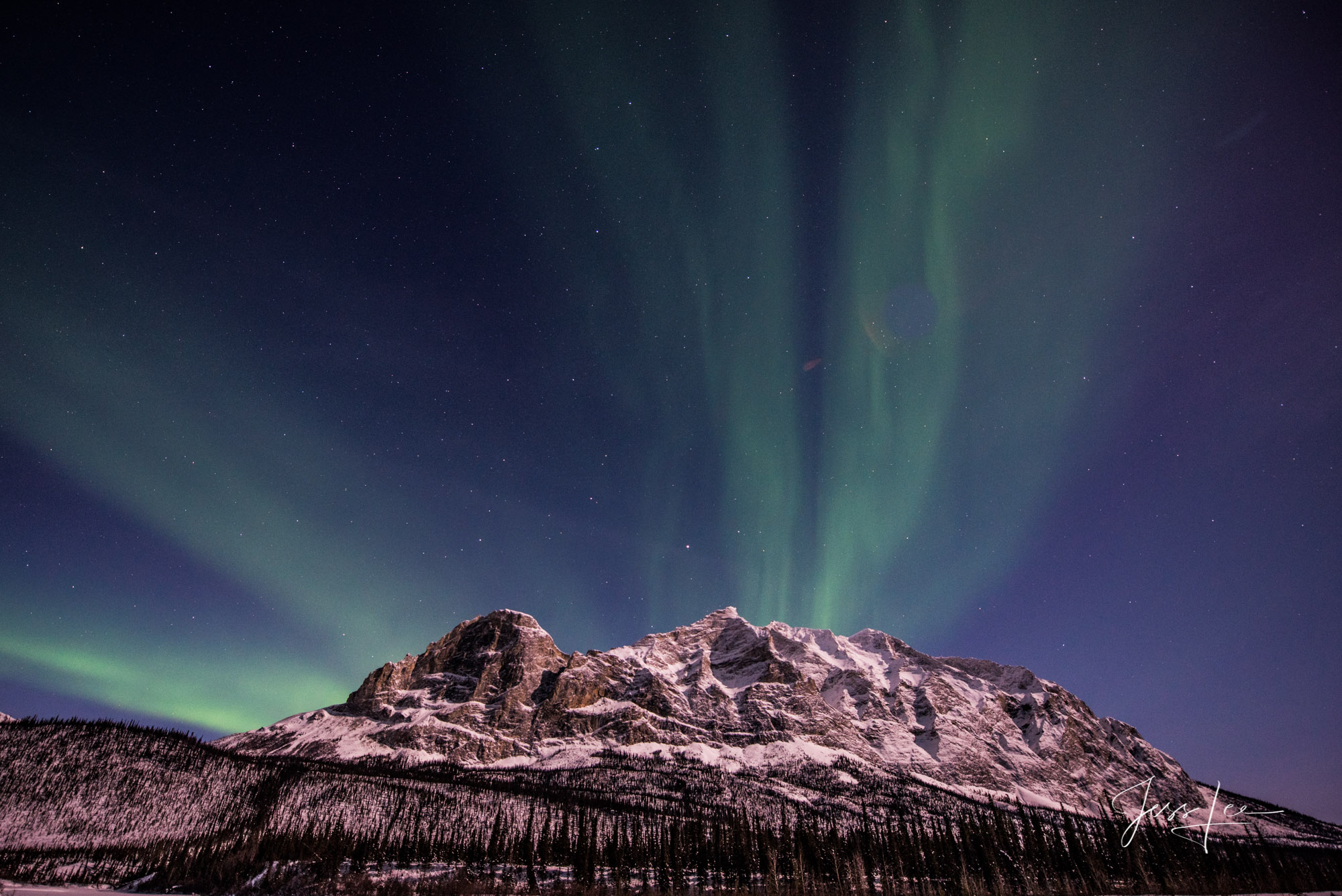 Mountain range in Alaska with the aurora borealis putting on a show behind it. 