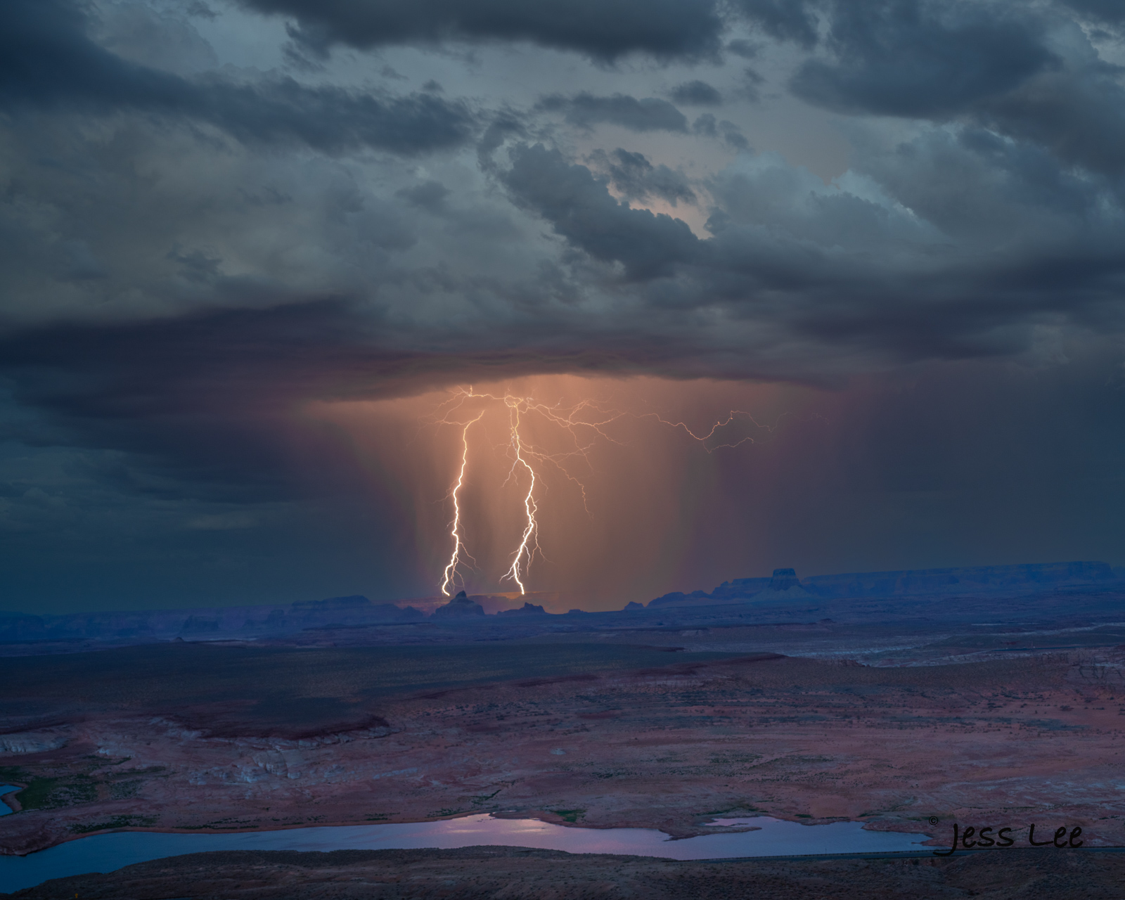 Twin lightning strikes on twin peaks beyond Lake Powell in the Navajo Reservation. This rare photograph was captured after many...
