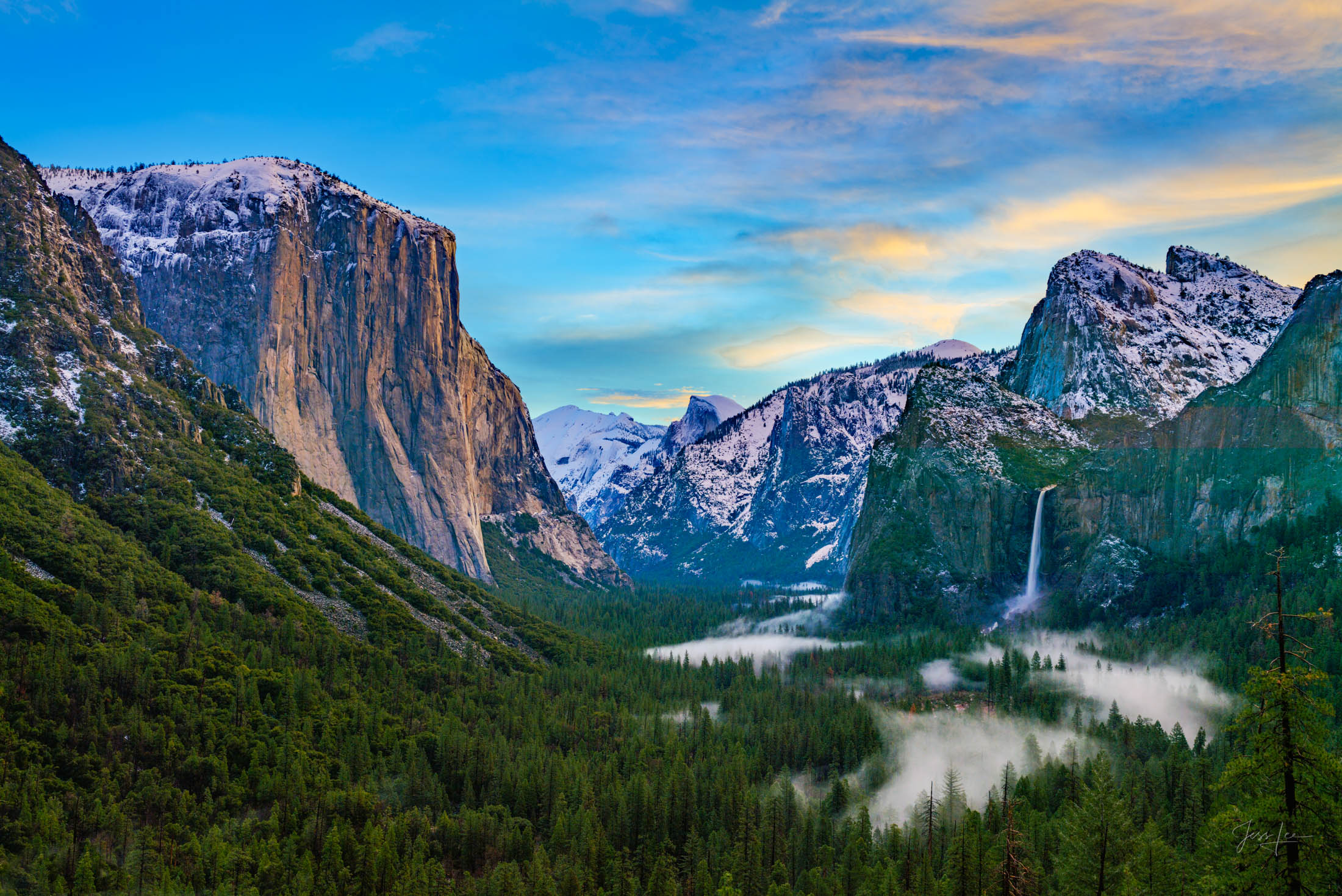 An early morning capture of the serene Yosemite Valley, adorned with patches of ethereal fog and wispy clouds against a clearing...